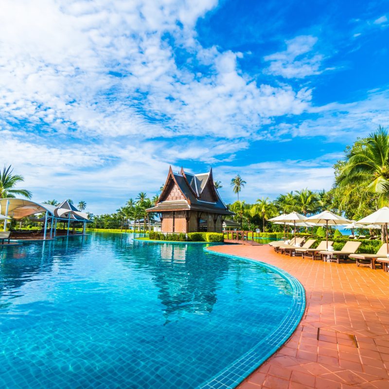Beautiful luxury umbrella and chair around outdoor swimming pool in hotel and resort with coconut palm tree on blue sky - Boost up color Processing